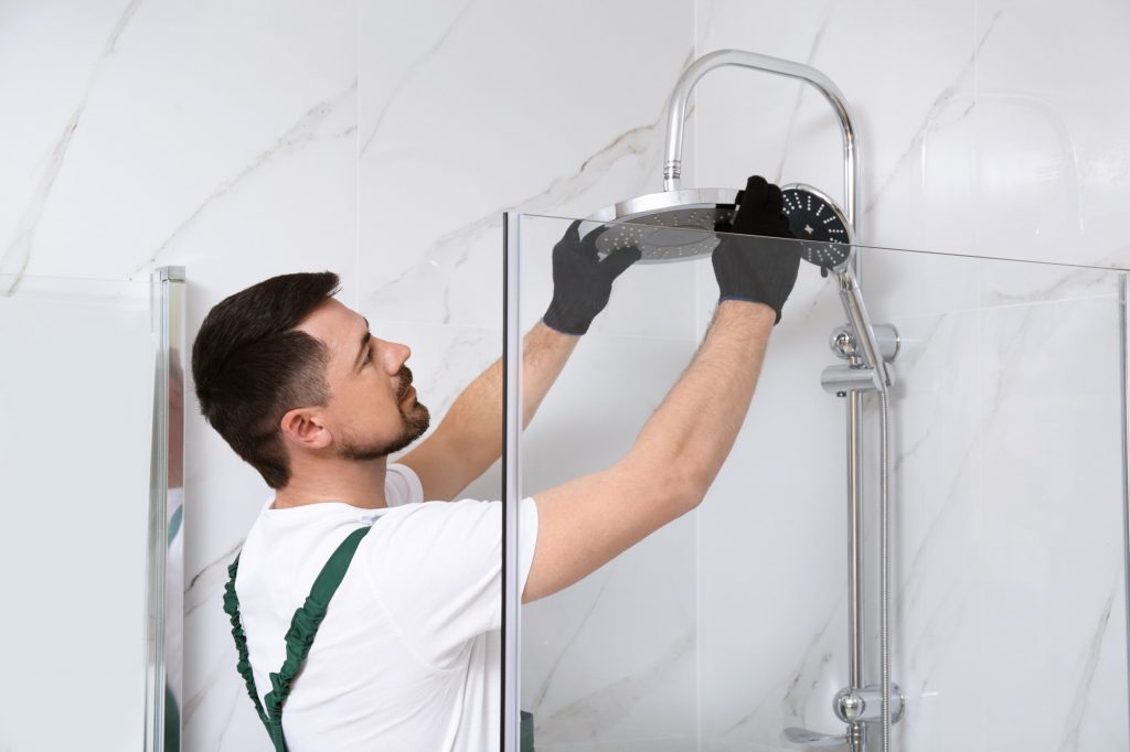 Handwerker montiert einen Duschkopf hinter einer Glaswand.