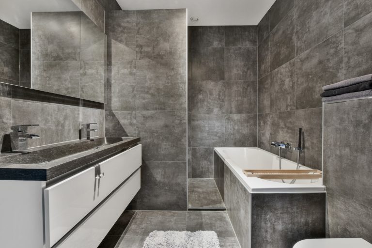 Bad mit grauen Fliesen, Waschtisch, Dusche und Badewanne.
