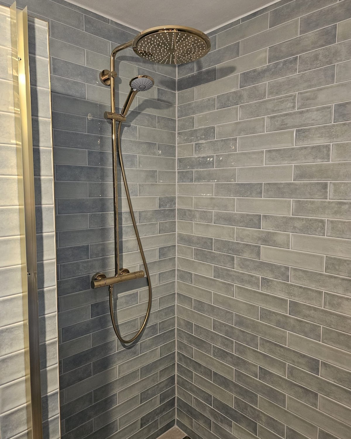 Regendusche in Messing vor grauen Wandfliesen im Ziegelformat