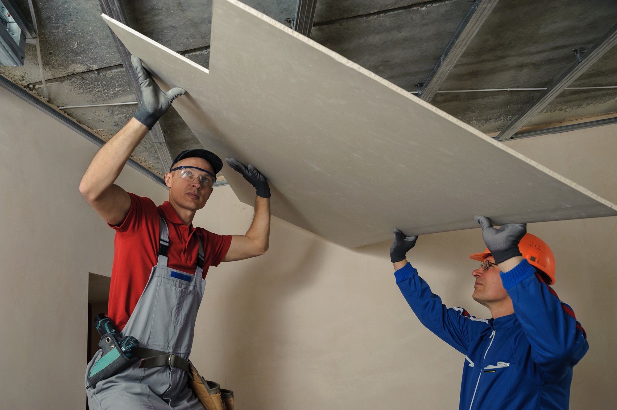 Zwei Handwerker montieren eine Gipskartonplatte an der Decke.